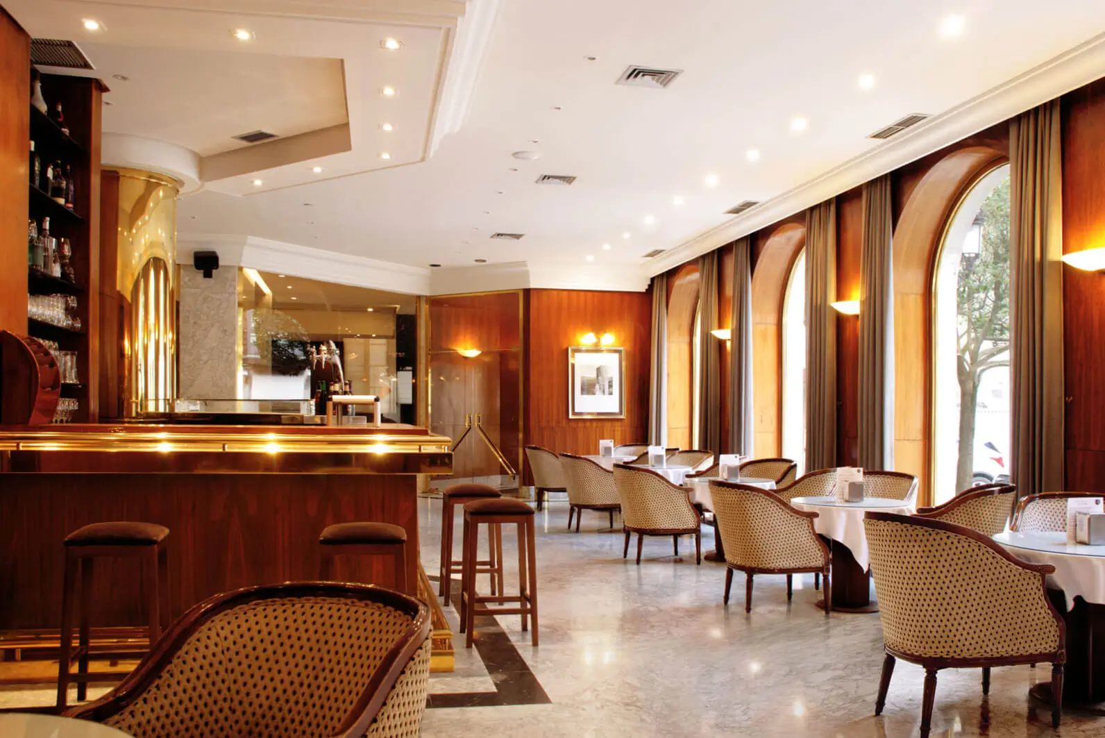 Interior de la cafetería del Hotel Mozart en Valladolid, con mesas redondas, sillas de estilo clásico y barra de madera.