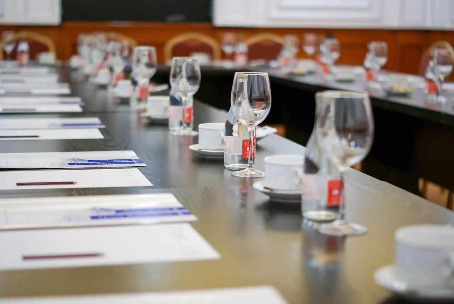 Primer plano de una mesa de reunión en el Hotel Mozart, con carpetas, bolígrafos, vasos y botellas de agua para los asistentes.