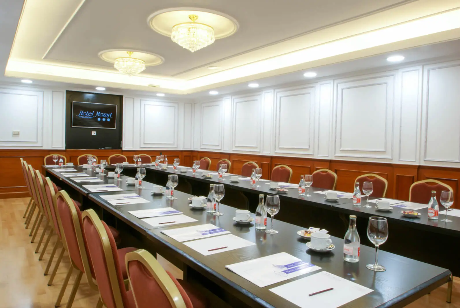 Salón de reuniones en el Hotel Mozart Valladolid con montaje en forma de U, equipado con pantalla, megafonía y servicio de aguas para empresas.