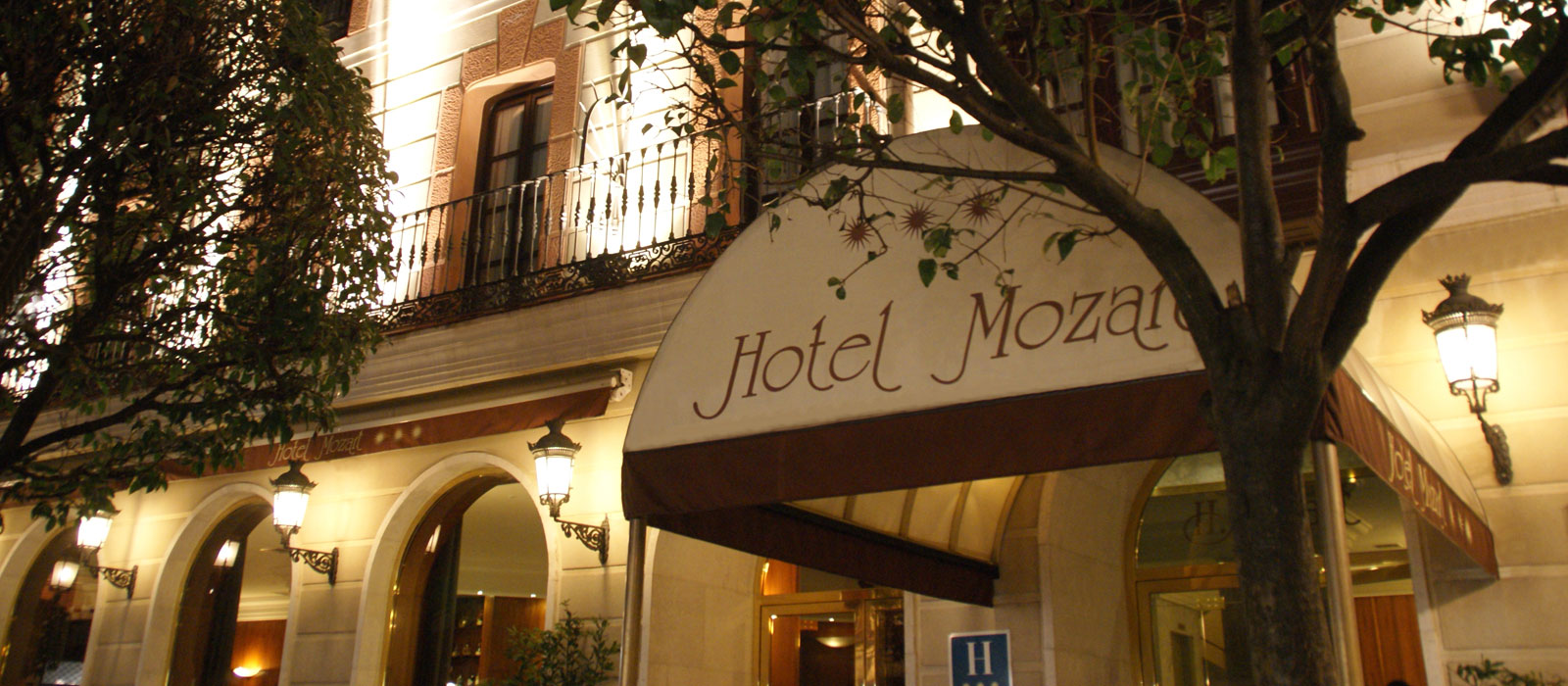 Entrada principal iluminada del Hotel Mozart en Valladolid de noche, destacando la marquesina clásica con el nombre del hotel.