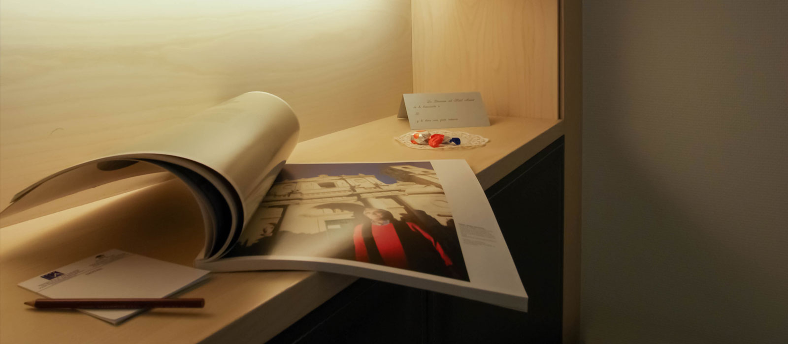 Escritorio de una habitación del Hotel Mozart Valladolid con una revista abierta, papelería y un detalle de bienvenida.